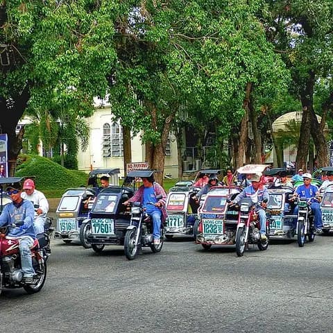 A row of motorised tricycles on a tree-lined avenue in the Philippines